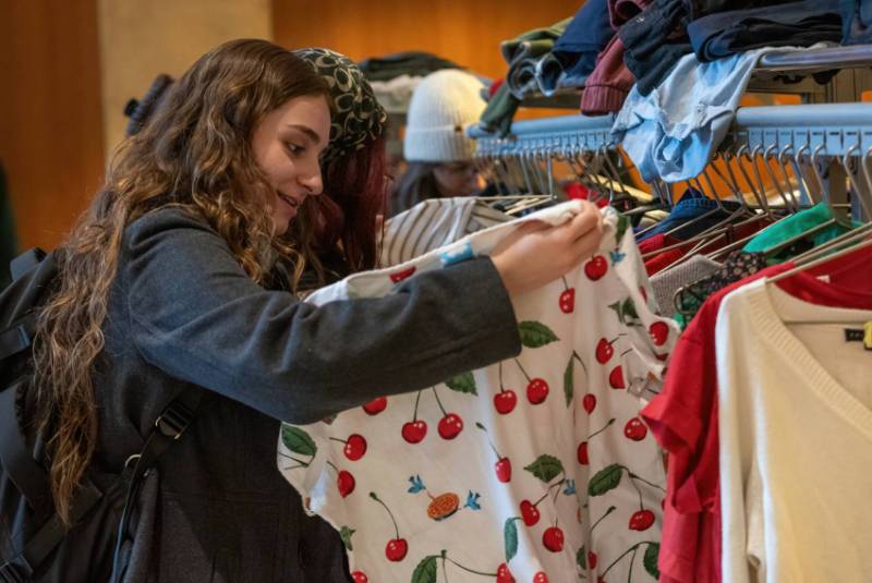 A student looks through a rack of clothing from the WCU thrift store, pausing on a cherry-patterned blouse.