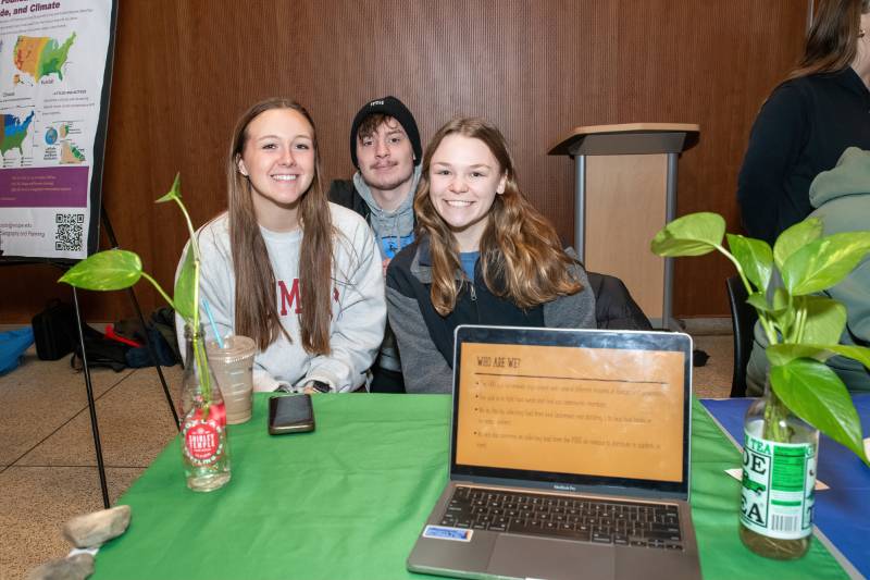 Three students smile sitting at a table for the Food Recovery Network