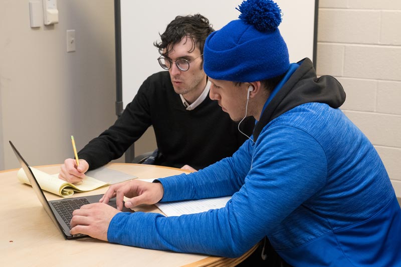 Two men sitting at a table looking at a laptop