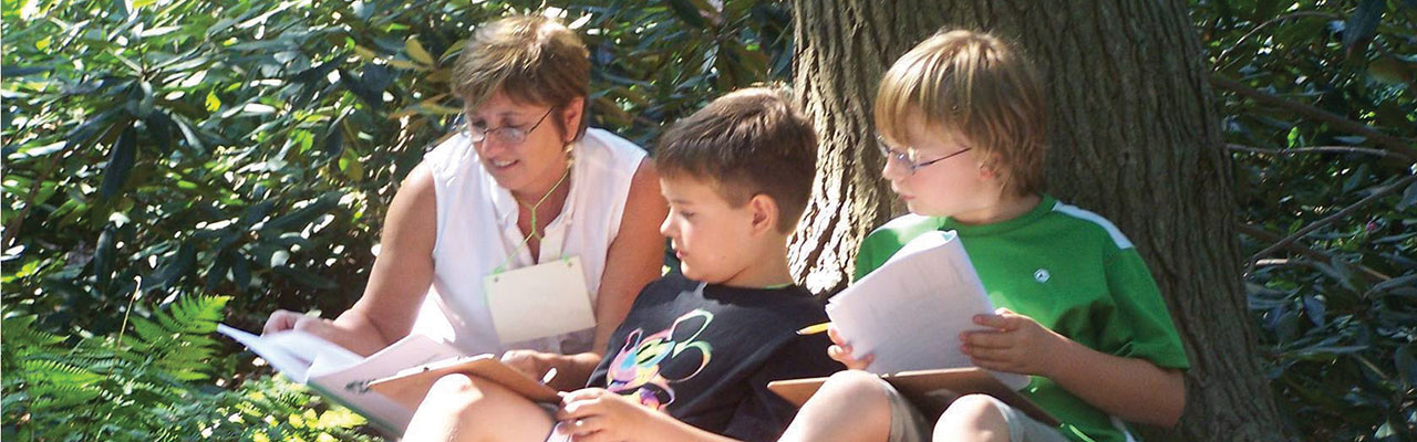 Teacher reading to two boys in front of tree