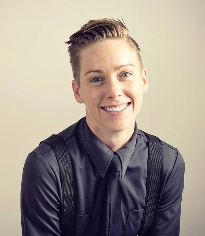 image of sam - white skin, short borwn hair, wearing a navy button up, tie, and suspenders with a beige background 