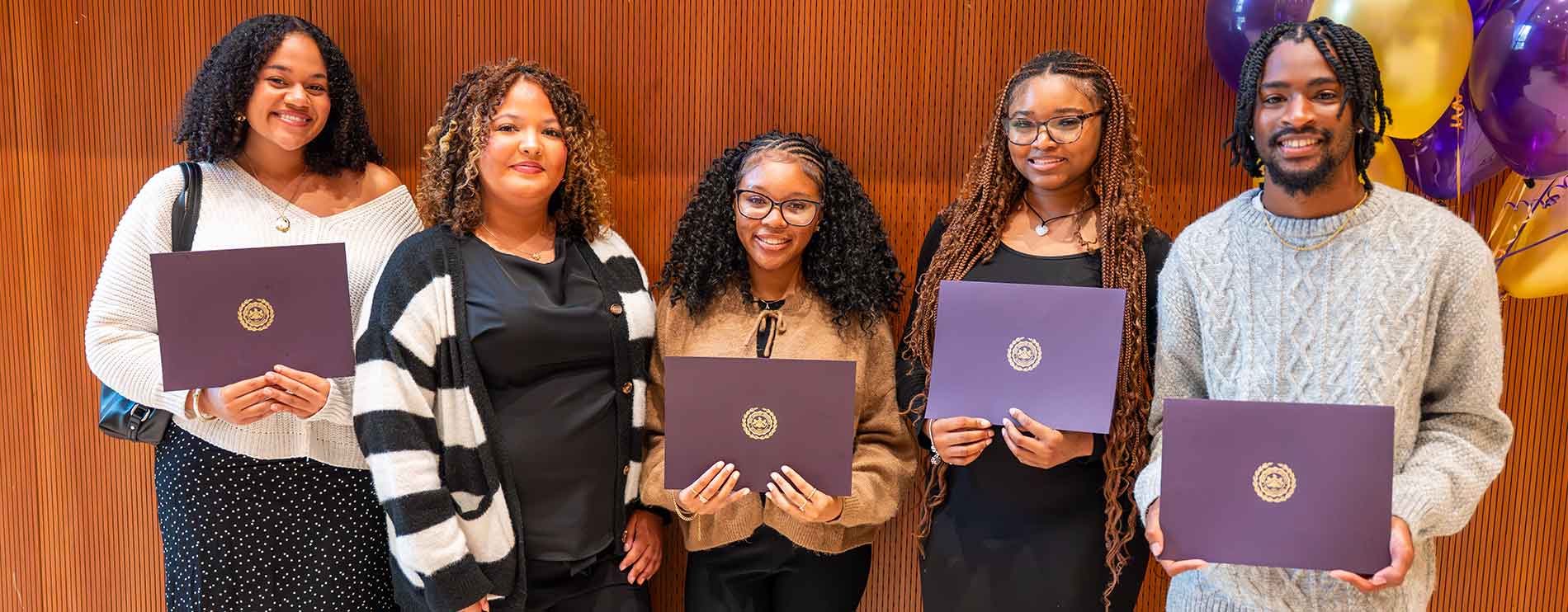Group of 5 students holding their diploma folders