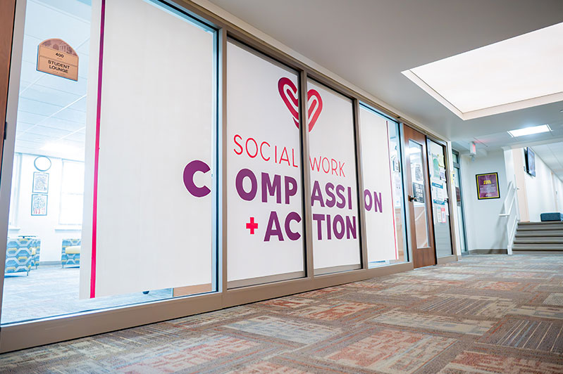 A large sign over a glass wall that says Social Work is Compassion + Action
