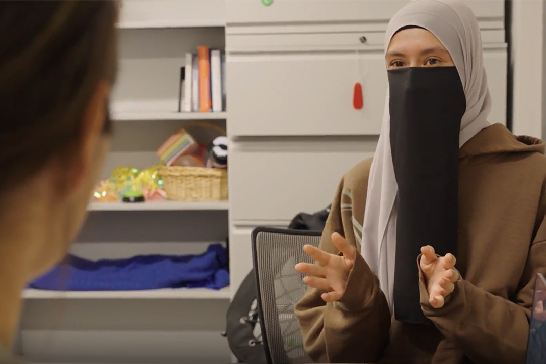 Woman in hijab speaking with blurred figure