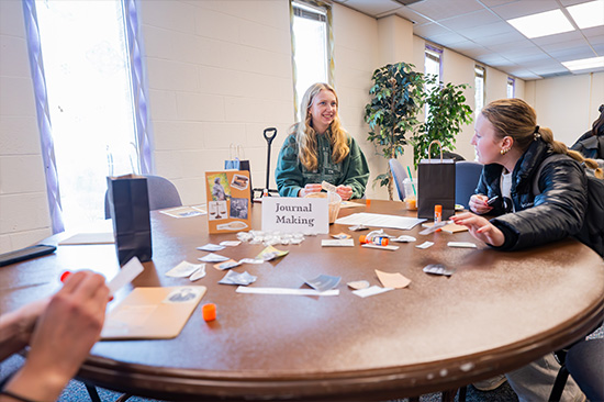 Candid photo from the Frederick Douglass day event. 2 female students working at 'journal making' table.